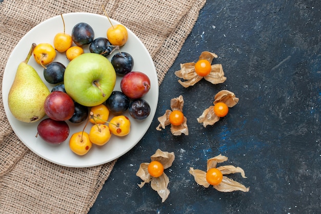 Top view of different fresh frutis pear plums blackthorns and apple inside plate on dark desk, fruit fresh food snack health vitamine