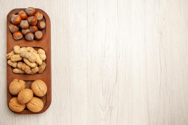 Top view different fresh nuts peanuts hazelnuts and walnuts on a white desk nut snack many plant