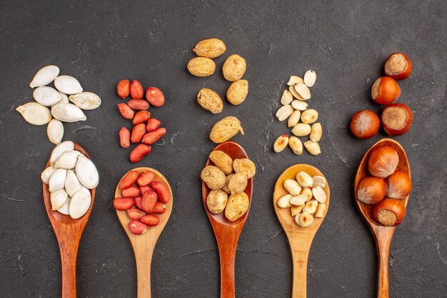 Top view of different fresh nuts peanuts and other nuts on spoons on dark surface