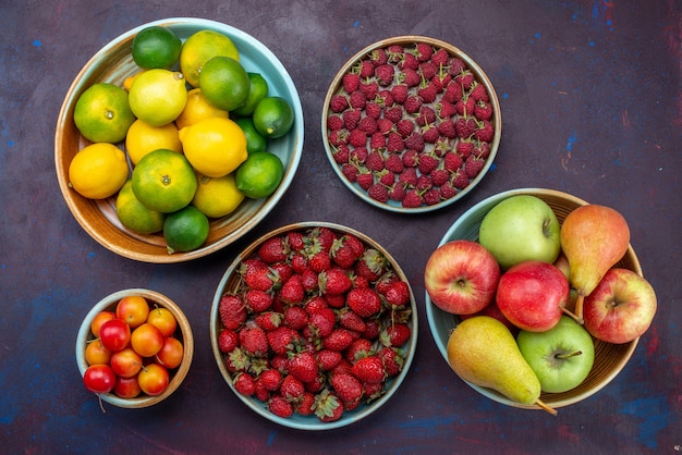 Vista dall'alto diversi frutti bacche e agrumi sulla scrivania scura agrumi esotici tropicali di frutta arancione