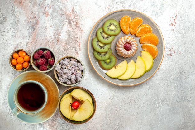 Вид сверху различных фруктов, состав, свежие фрукты с тортом и чашкой чая на белом фоне, спелые фрукты, спелые витамины, здоровье