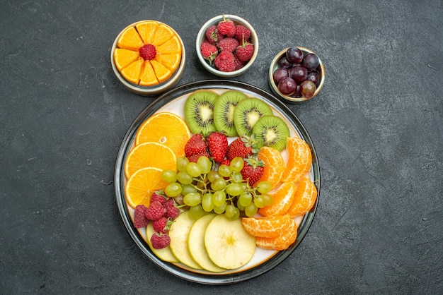 Free photo top view different fruits composition fresh and sliced fruits on dark background health ripe fresh fruits mellow