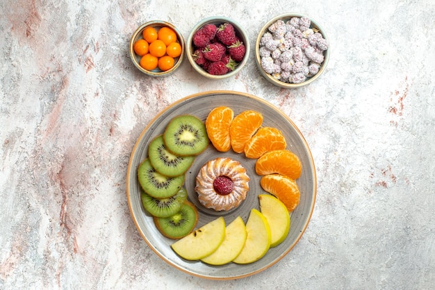 Вид сверху разных фруктов, свежие и нарезанные фрукты с тортом на белом столе, спелые фрукты, здоровье, спелые витамины