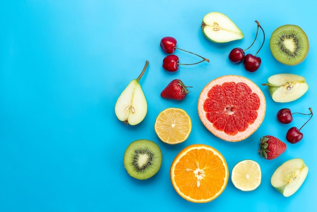 Вид сверху на разные фруктовые композиции, нарезанные свежими на синем, фруктовом цитрусовом цвете витамина