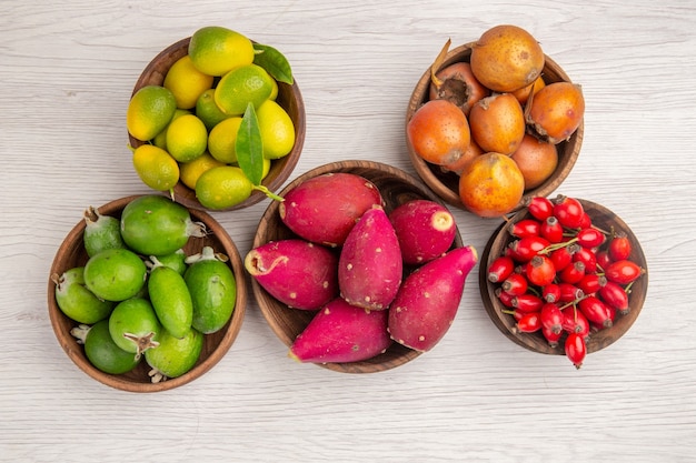 Вид сверху различных фруктов фейхоа и других фруктов внутри тарелок на белом фоне здоровая спелая еда экзотического цвета тропическое дерево
