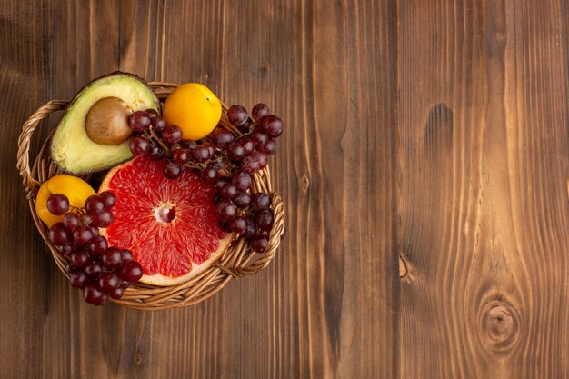 Top view different fruits inside basket on brown wooden desk