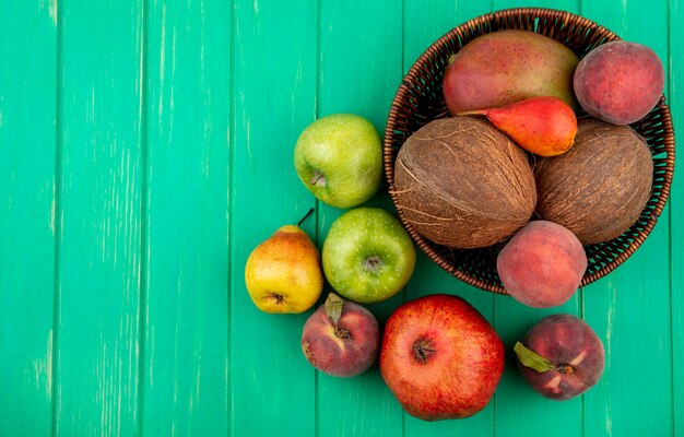 Top view of different fruits like coconut apple peach pear on bucket on green