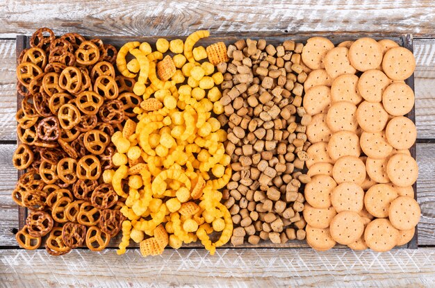 Top view of different kind of snacks as crackers and cookies on white wooden  horizontal