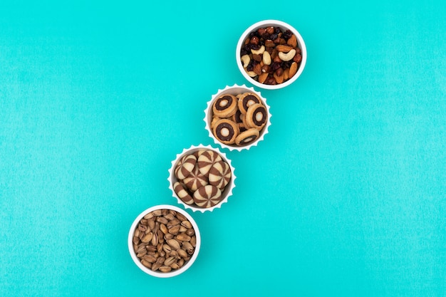 Top view of different kind of snacks as nuts and coockies in bowls on blue  horizontal