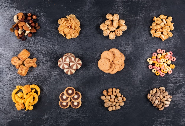 Top view of different kind of snacks as nuts, crackers and coockies on dark  horizontal