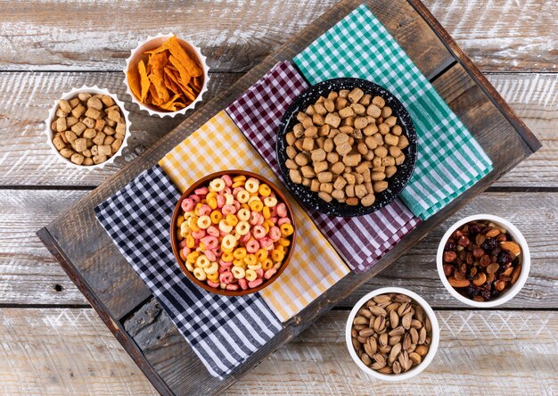 Вид сверху различных видов закусок, как орехи, крекеры и печенье на салфетках на белой деревянной поверхности горизонтальной