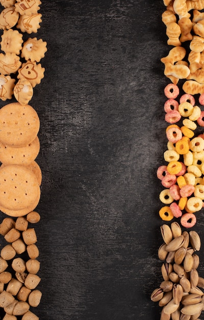 Vista superiore del tipo differente di spuntini come dadi, cracker e biscotti con lo spazio della copia sul verticale scuro del fondo