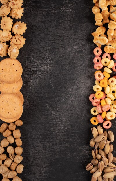 Top view of different kind of snacks as nuts, crackers and cookies with copy space on dark background vertical