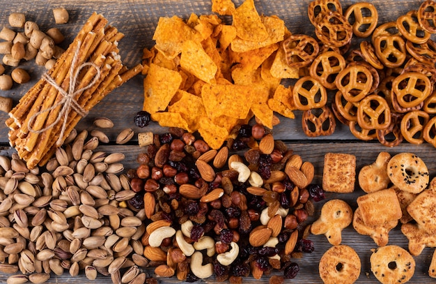 Top view of different kind of snacks as nuts, crackers and cookies with copy space on dark wooden surface horizontal