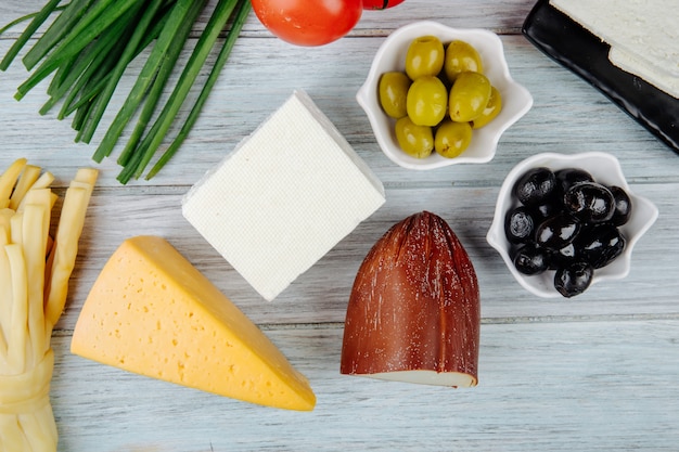 Top view of different kinds of cheese with green onion and pickled olives on grey wooden table