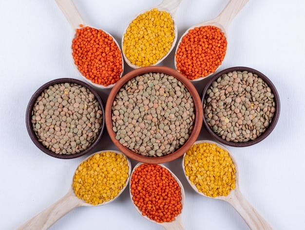 Top view different lentils in brown bowls and wooden spoons