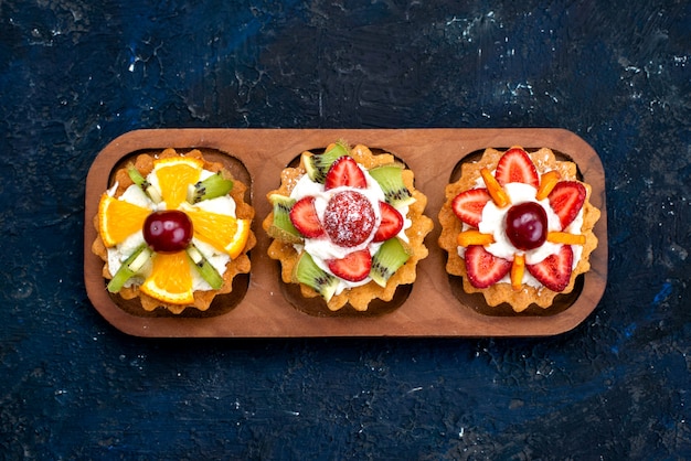 Foto gratuita una vista dall'alto diversi piccoli dolci con crema e frutta fresca a fette sul tè biscotto torta di frutta sfondo blu