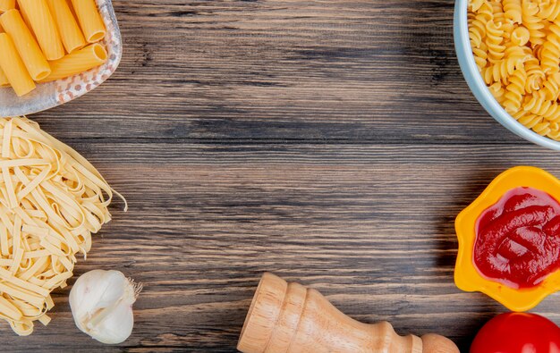 Top view of different macaronis as ziti rotini tagliatelle with ketchup tomato garlic on wood with copy space