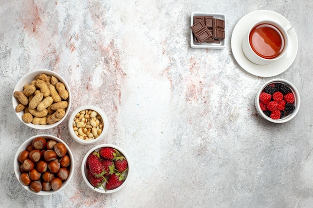 Top view of different nuts hazelnuts peanuts and cup of tea on white surface