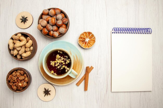 Top view different nuts inside little pots with cup of tea on a white desk nut snack walnut hazelnut