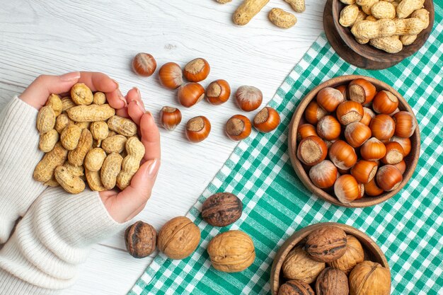 Top view different nuts peanuts hazelnuts and walnuts on white table in female hand