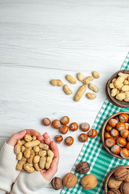 Top view different nuts peanuts hazelnuts and walnuts on white table in female hand