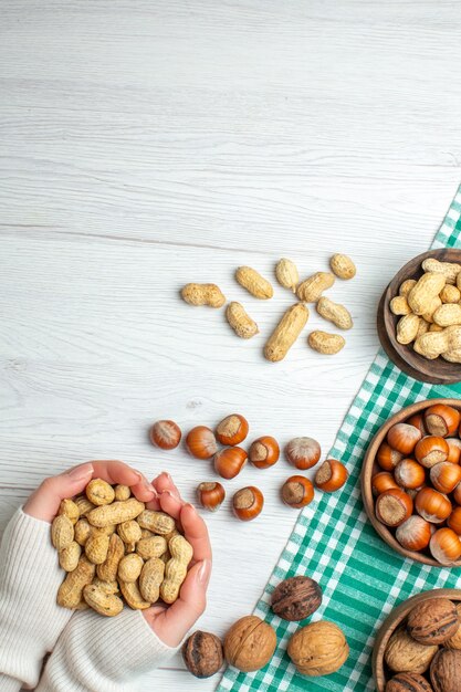 Top view different nuts peanuts hazelnuts and walnuts on white table in female hand