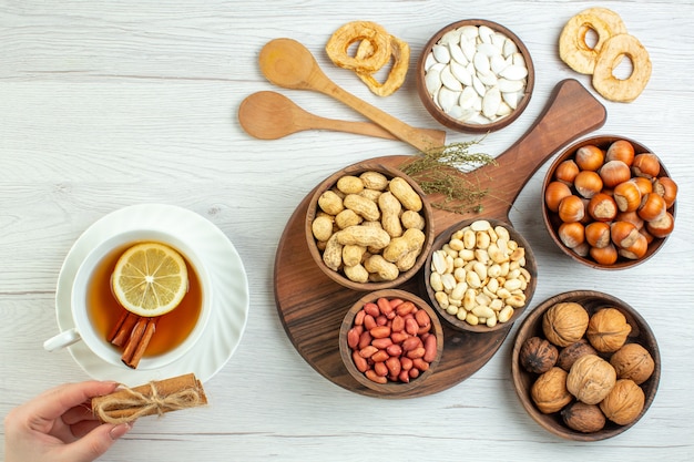 Top view different nuts peanuts hazelnuts and walnuts with cup of tea on white table