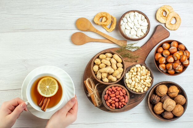 Top view different nuts peanuts hazelnuts and walnuts with cup of tea on white table