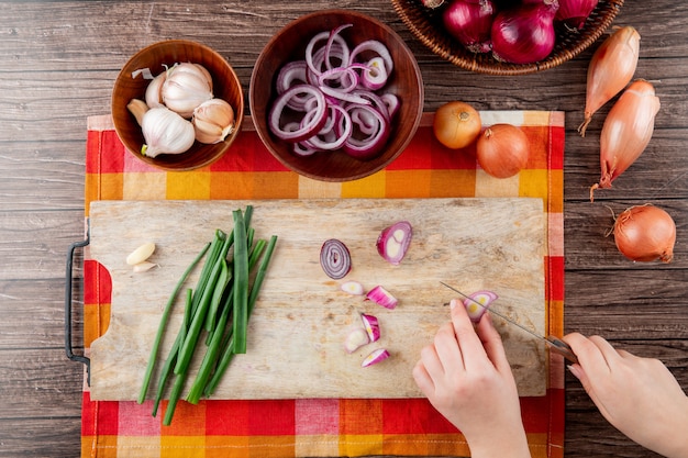 Top view of different onions and garlic with woman hand cutting onion on wooden background