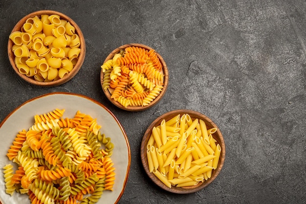 Top view of different pasta composition raw product inside plates on grey pasta raw cooking dough meal