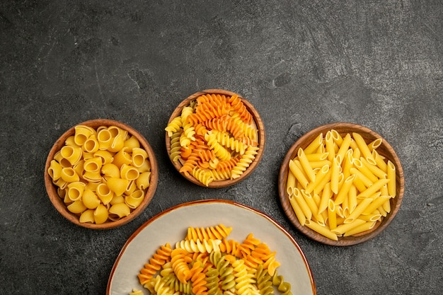 Top view of different pasta composition raw product inside plates on grey