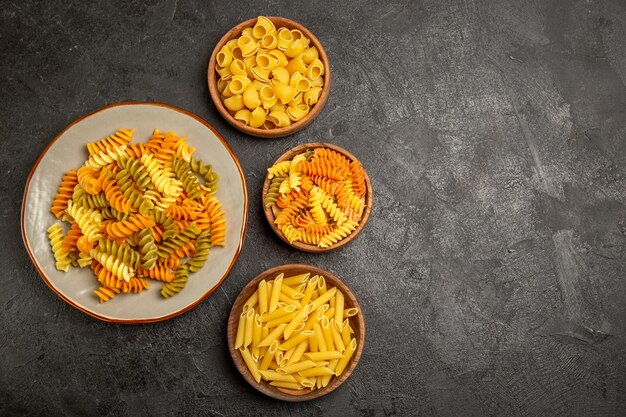 Top view of different pasta composition raw product inside plates on grey