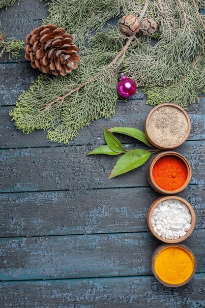 Top view different seasonings inside little pots on dark-blue rustic desk spicy edgy pepper color