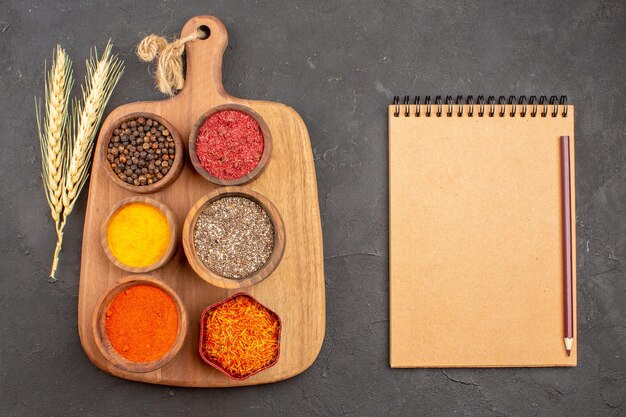 Top view of different seasonings spicy ingredients inside pots with notepad on black