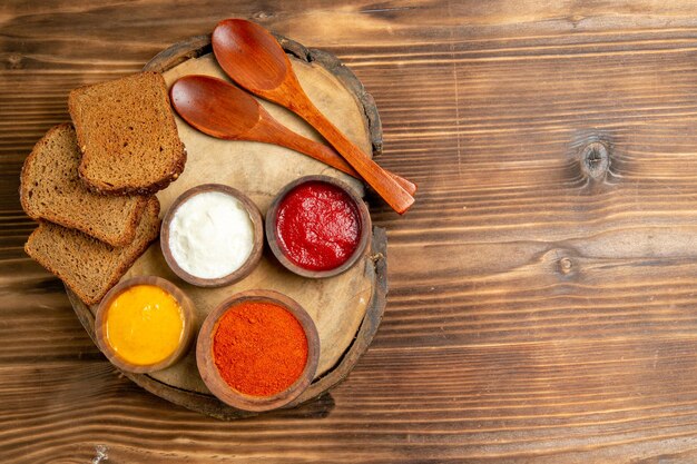 Top view of different seasonings with black bread loafs on brown table