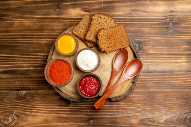 Top view of different seasonings with black bread loafs on brown wooden table