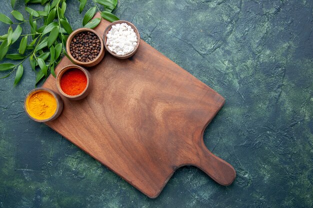 Top view different seasonings with brown wooden desk on dark-blue surface color sharp cutlery tree green kitchen