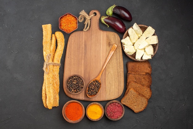 Top view of different seasonings with cheese and black bread loafs on black