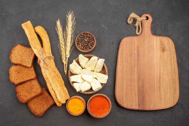 Top view of different seasonings with cheese and black bread loafs on black