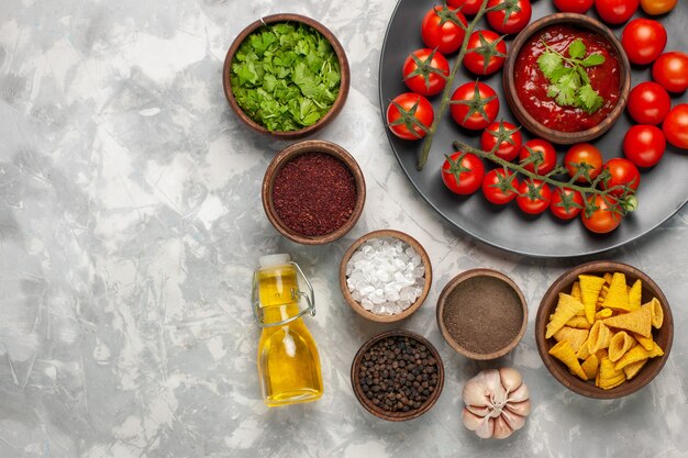 Top view different seasonings with cherry tomatoes and oil on white desk