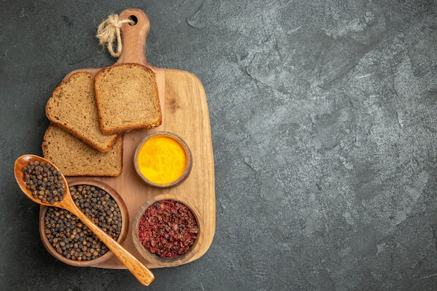 Top view different seasonings with dark bread loafs on grey desk bread spicy hot