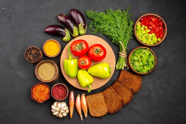 Вид сверху разные приправы с зеленью, овощами и темными буханками хлеба на темном фоне приправы для салата хлеб здоровая еда