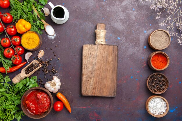 Top view different seasonings with greens and vegetables on a dark space