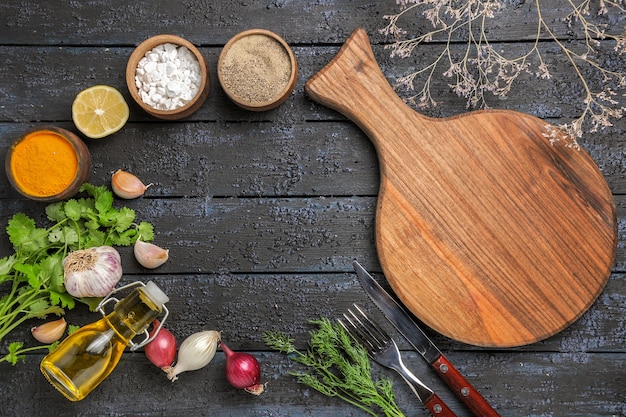 Top view different seasonings with oil and greens on dark desk