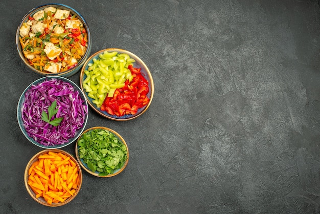 Top view different sliced vegetables with greens on a dark table health diet salad