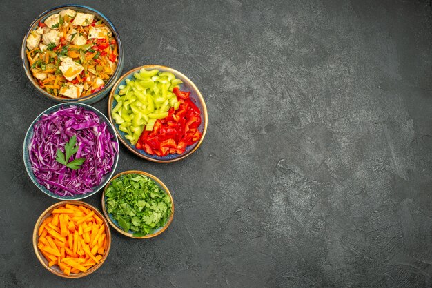 Top view different sliced vegetables with greens on a dark table health diet salad