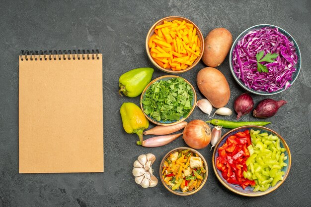 Top view different sliced vegetables with greens on dark table health meal diet