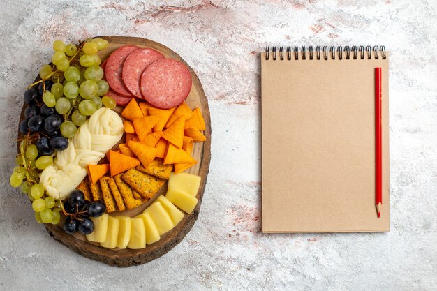 Top view different snacks cips sausages cheese and fresh grapes on light white space