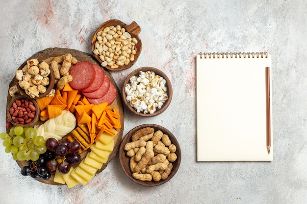 Vista dall'alto diversi snack noci cips uva formaggio e salsicce su uno sfondo bianco chiaro dado spuntino frutta